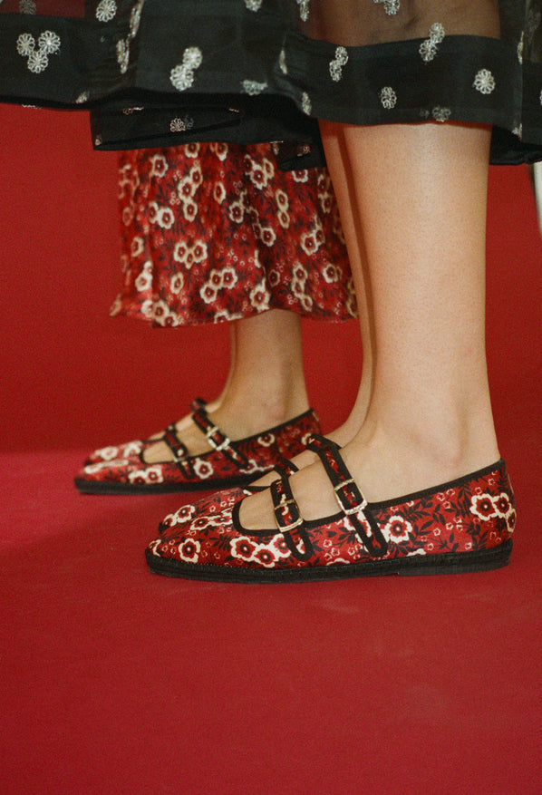 Shin down crop of two women wearing red floral-patterned shoes against a red sleamless
