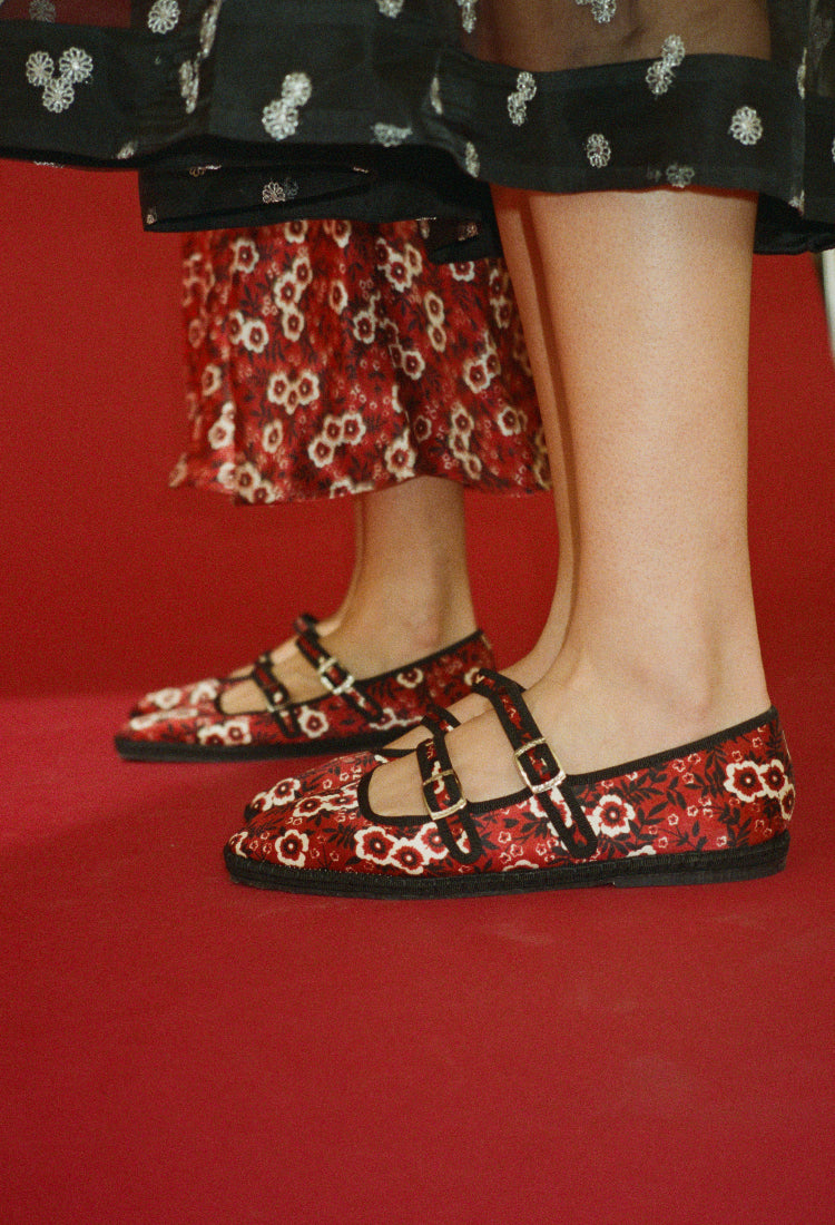 Shin down crop of two women wearing red floral-patterned shoes against a red sleamless