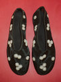 Sheer slip on black flats with mini white floral embroidery detail against a red background. 