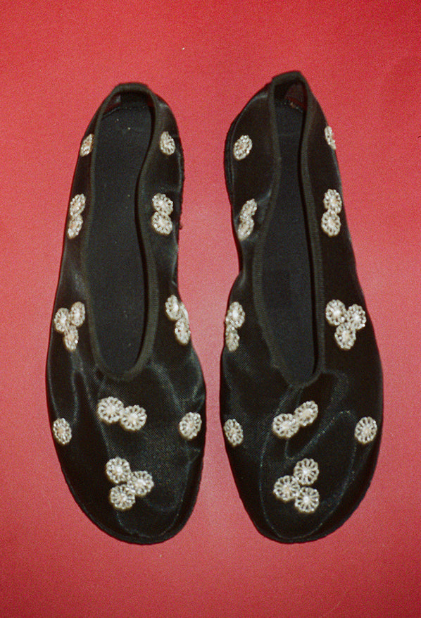 Sheer slip on black flats with mini white floral embroidery detail against a red background. 