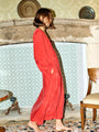 Woman in a red caftan dress standing in a room with decorative tiles and a fireplace.