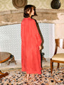 Woman in a red caftan dress standing in an ornate room with patterned wallpaper and floor.