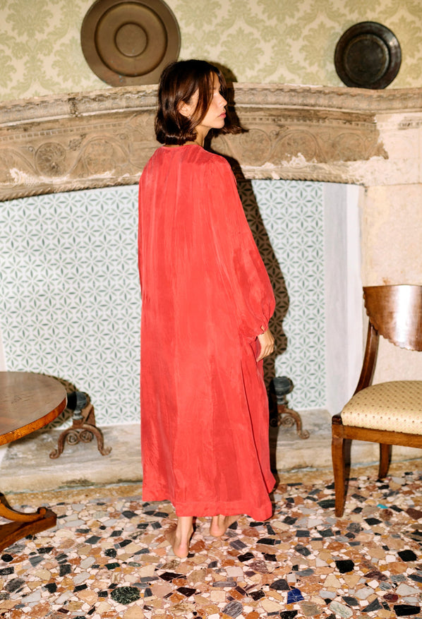 Woman in a red caftan dress standing in an ornate room with patterned wallpaper and floor.