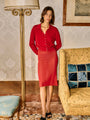 Woman in a red button up cardigan and red sheer midi skirt standing in an elegant room with a lamp and sofa.