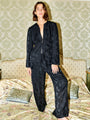 Person wearing a black floral long sleeve blouse with matching pants standing on a bed in a room with patterned wallpaper.