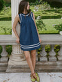 Woman in a sleeveless blue short dress with white neck, sleeve, and hem detailing standing in a garden setting