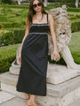 Woman in a black midi length tank dress with lace bodice and white embroidered ruffle trim details standing outdoors near a stone lion sculpture.