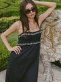 Cropped knees up of woman in a black midi length tank dress with lace bodice and white embroidered ruffle trim details standing outdoors near a stone lion sculpture.