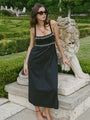 Woman in a black midi length tank dress with lace bodice and white embroidered ruffle trim details standing outdoors near a stone lion sculpture.