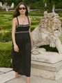Woman in a black midi length tank dress with lace bodice and white embroidered ruffle trim details standing outdoors near a stone lion sculpture.