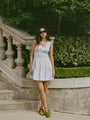 Woman in a light blue pin-striped tank style mini dress with a smocked bodice standing outdoors with greenery in the background