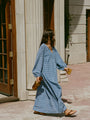 Woman in a long sleeve blue zigzag print Caftan dress walking outside a building. 