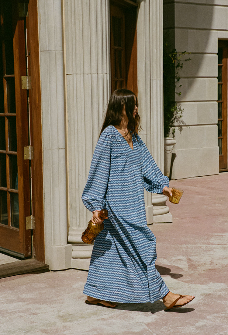 Woman in a long sleeve blue zigzag print Caftan dress walking outside a building. 