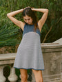 Cropped shin up of woman in a striped white and navy tank style knit dress standing outdoors against a stone railing with greenery.