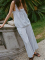 Cropped chin down of woman in light blue pin-striped sleeveless top and matching wide-leg pants leaning on a stone railing outdoors.