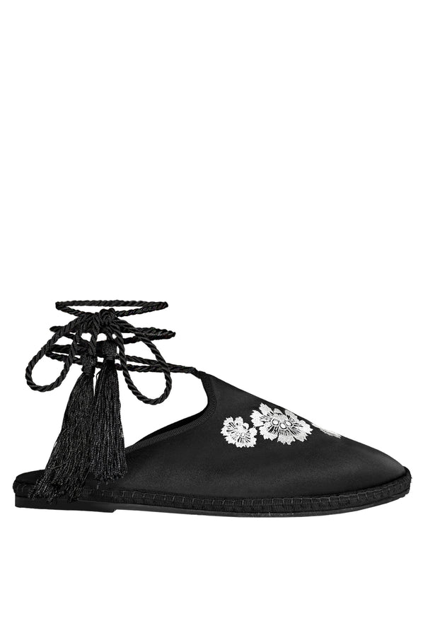 Black slip-on shoes with white floral embroidered in the top and twist-cord ties with tassels to wrap around the ankle on a white background