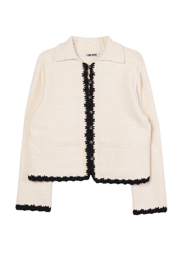 Ivory knit jacket with black trim detailing along the sleeves, hem, and center seam against a white background