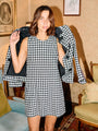 Cropped image of woman wearing a black and white checkered gingham jacket with matching mini dress in a room with vintage decor.