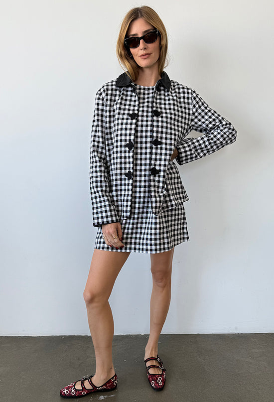 Woman wearing a black and white checkered gingham jacket and matching mini dress against a plain background