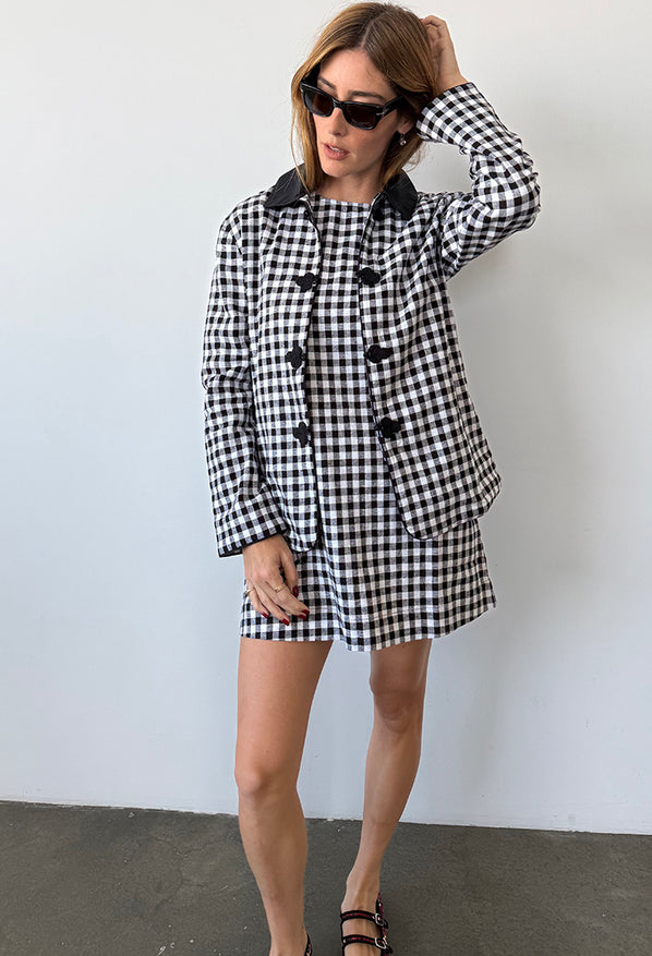 Woman wearing a black and white checkered gingham jacket and matching mini dress against a plain background