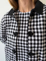 Cropped chin to stomach image of woman wearing a black and white checkered gingham jacket with black embroidered buttons and collar with matching under dress on a plain background