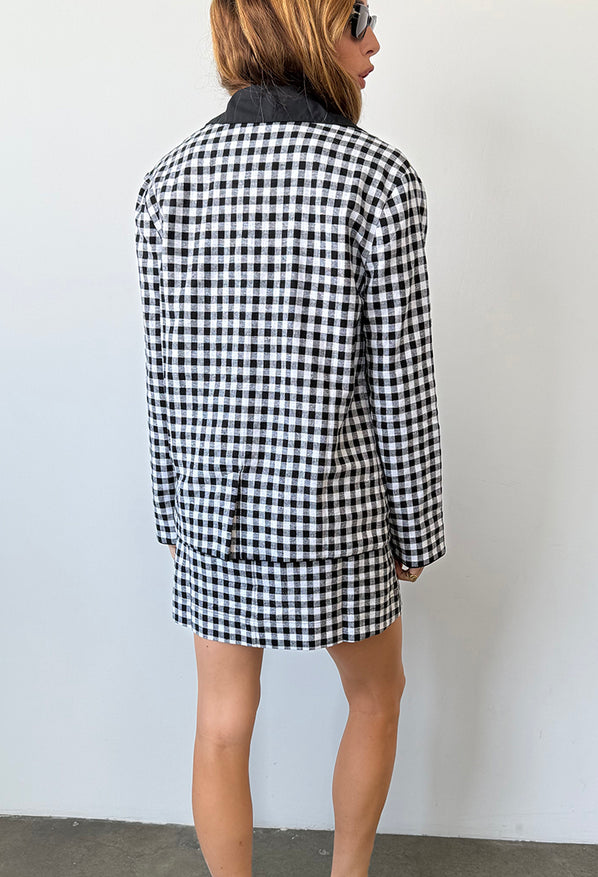 Cropped image from behind view of woman wearing a black and white checkered gingham jacket and matching mini dress against a plain background