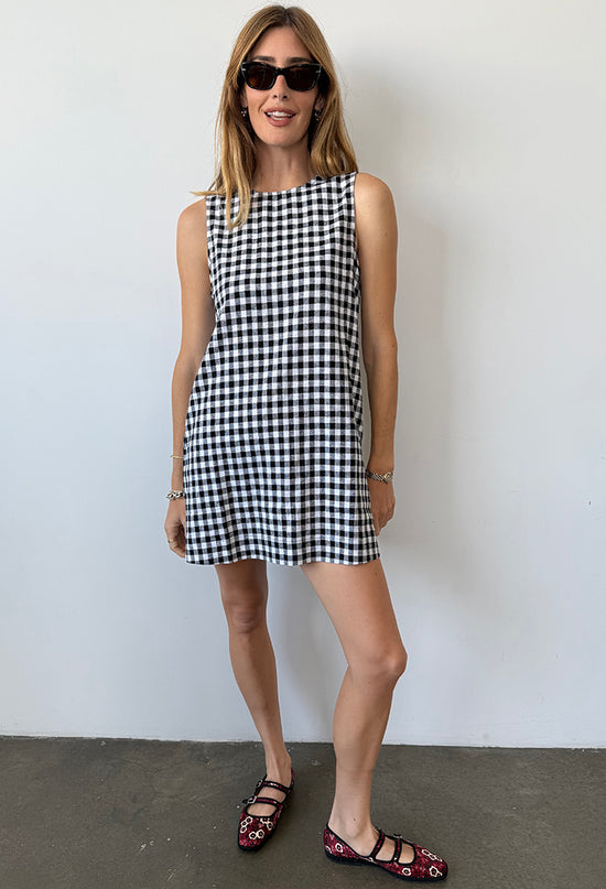Woman wearing a black and white checkered gingham mini dress against a plain background