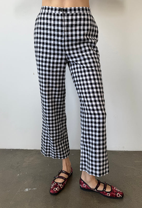 Cropped waist down of woman wearing black and white checkered gingham pants with floral shoes on a plain background