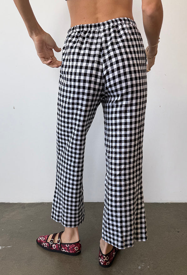 Cropped waist down behind view of woman wearing black and white checkered gingham pants with floral shoes on a plain background
