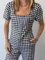 Cropped neck to thigh of woman wearing a black and white checkered gingham short sleeve top with matching pants against a plain background