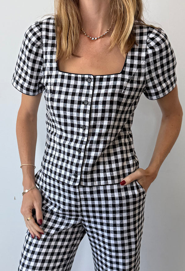 Cropped neck to thigh of woman wearing a black and white checkered gingham short sleeve top with matching pants against a plain background