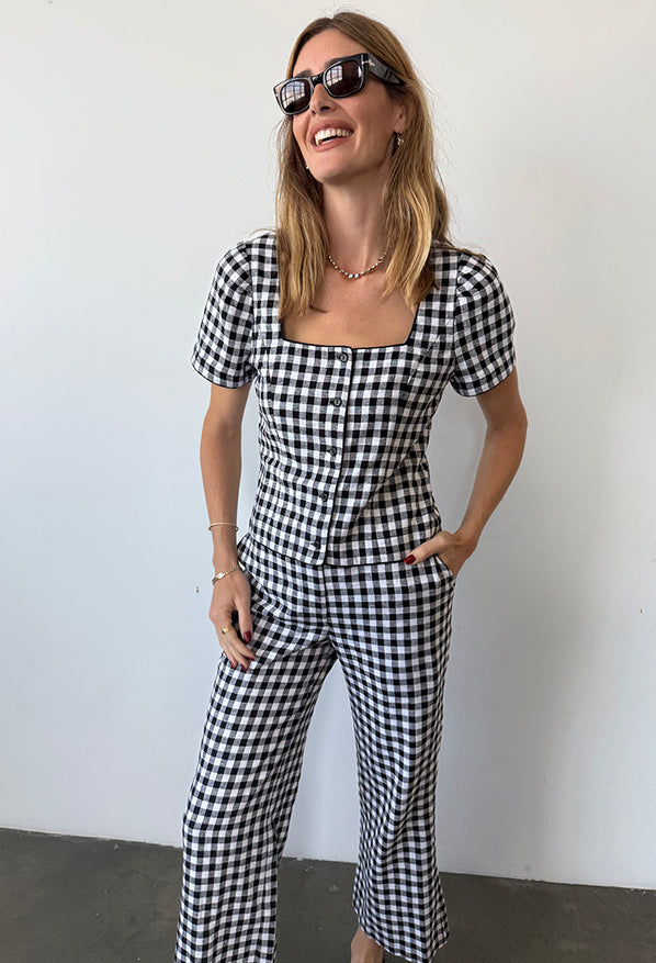 Image cropped at the ankles of woman wearing a black and white checkered gingham short sleeve top with matching pants against a plain background