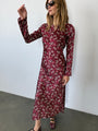 Woman wearing a silky midi length long sleeve ruby floral print dress against a plain background