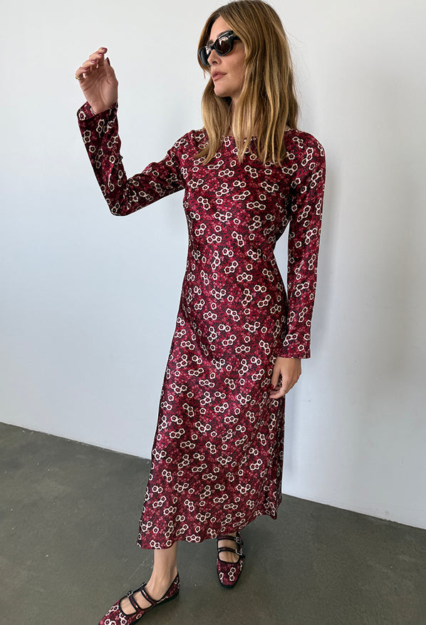 Woman wearing a silky midi length long sleeve ruby floral print dress against a plain background
