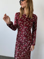 Cropped image of woman wearing a silky midi length long sleeve ruby floral print dress against a plain background
