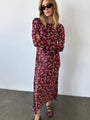 Woman wearing a silky midi length long sleeve ruby floral print dress against a plain background