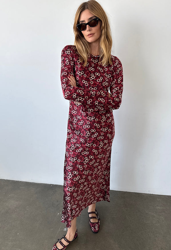 Woman wearing a silky midi length long sleeve ruby floral print dress against a plain background