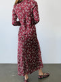 Back view cropped chin down of woman wearing a silky midi length long sleeve ruby floral print dress against a plain background