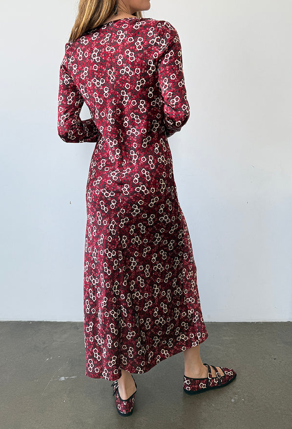 Back view cropped chin down of woman wearing a silky midi length long sleeve ruby floral print dress against a plain background
