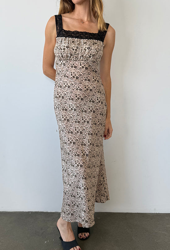 Cropped neck down of woman in a long silky sleeveless dress with floral cherry blossoms pattern with black lace neckline and straps against a white background