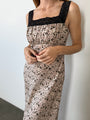 Cropped neck to thigh of woman in a long silky sleeveless dress with floral cherry blossoms pattern with black lace neckline and straps against a plain background. 
