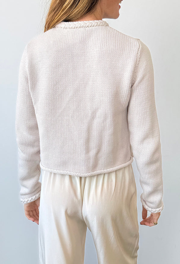 Woman wearing a beige-colored knit cardigan and pants against a light gray background