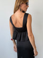 Image cropped at the thigh of woman wearing a cropped black sleeveless peplum top and a matching black satin skirt with floral embroidery on waist and hem against a white wall.