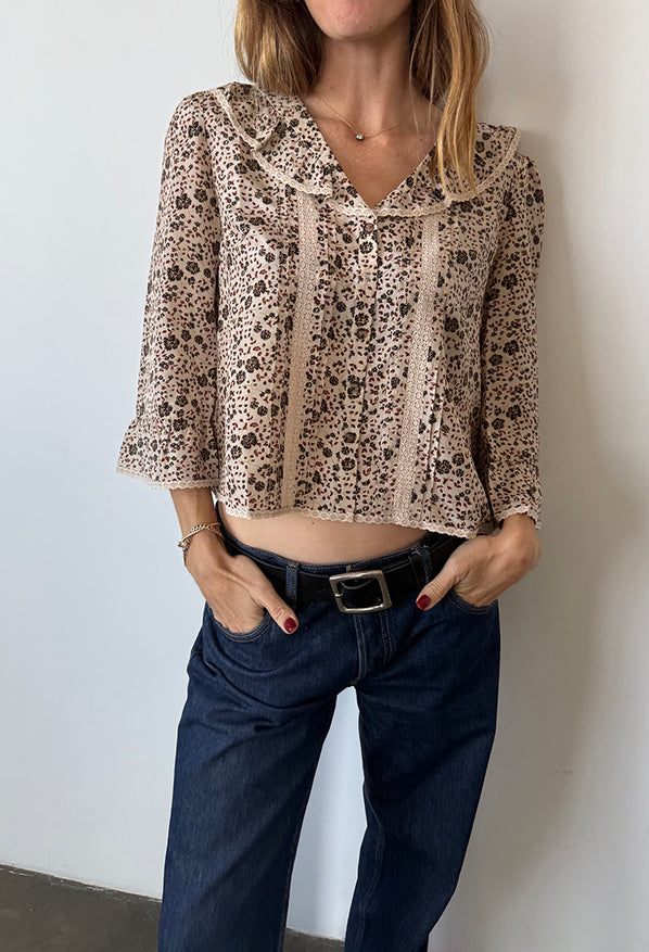 Cropped chin to knee of woman wearing a cherry blossom print patterned blouse with lace details down the front and jeans against a plain background