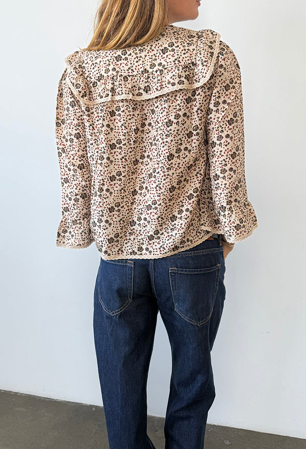 Back view cropped chin to calf of woman wearing a cherry blossom print patterned blouse with lace details down the front and jeans against a plain background