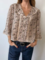 Cropped chin to thigh of woman wearing a cherry blossom print patterned blouse with lace details down the front and jeans against a plain background