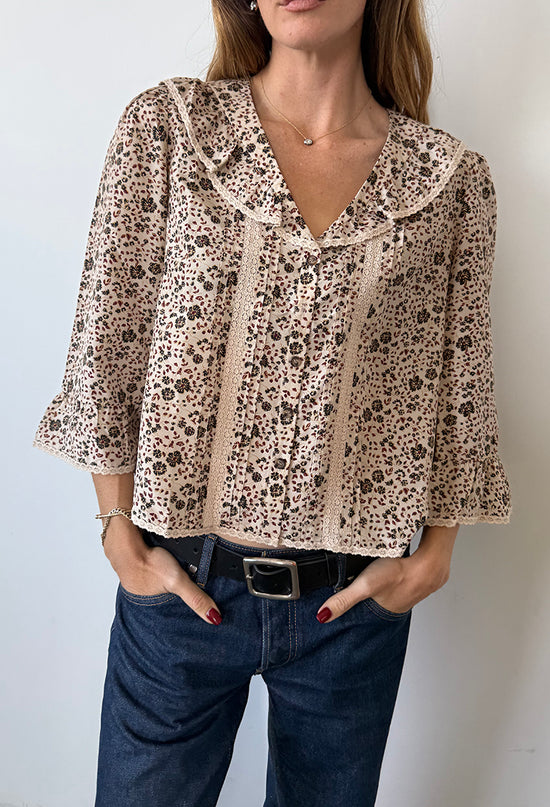 Cropped chin to thigh of woman wearing a cherry blossom print patterned blouse with lace details down the front and jeans against a plain background