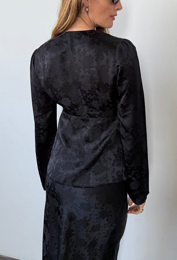 Cropped nose to thigh of woman wearing a black floral patterned long sleeve blouse with matching skirt against a white background