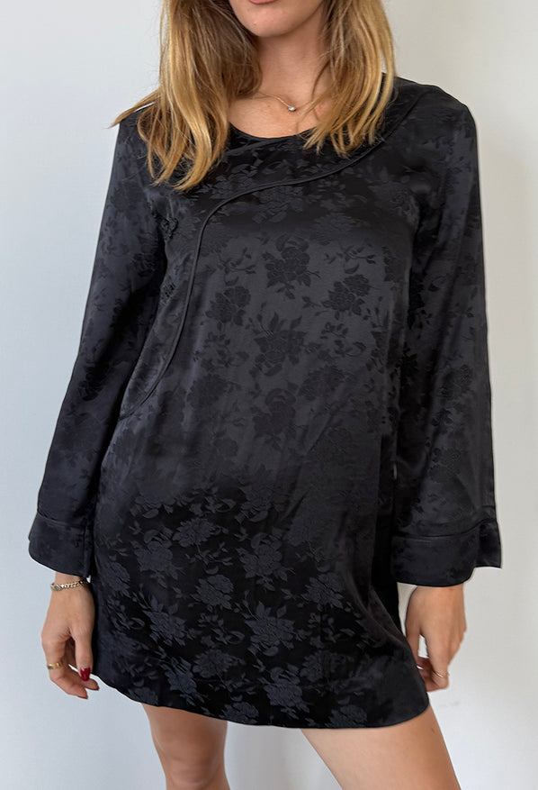 Cropped chin to knee of woman wearing a black floral patterned long sleeve mini dress against a white background