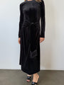 Cropped neck down of woman wearing a black velvet dress with long sleeves and front waist tie / tassels against a white background
